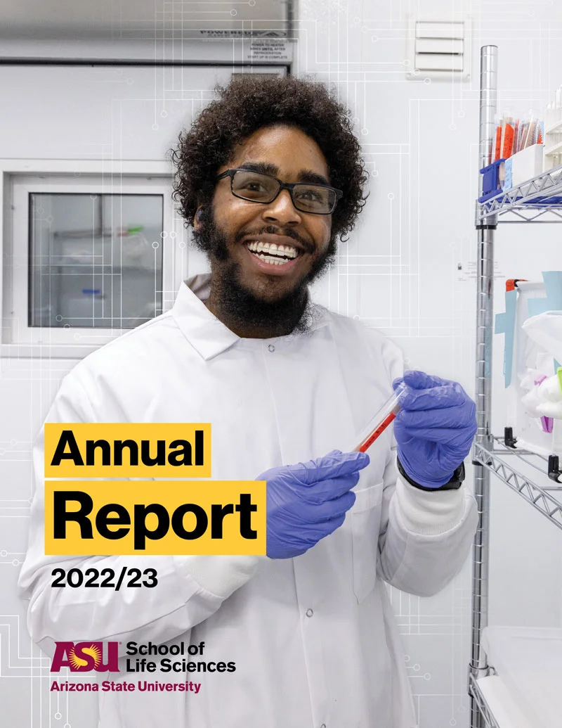 Black man wearing glasses and smiling holding a vial in his hands.