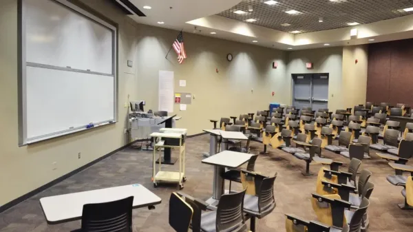 View of a classroom showing desks in rows a white board and a computer.